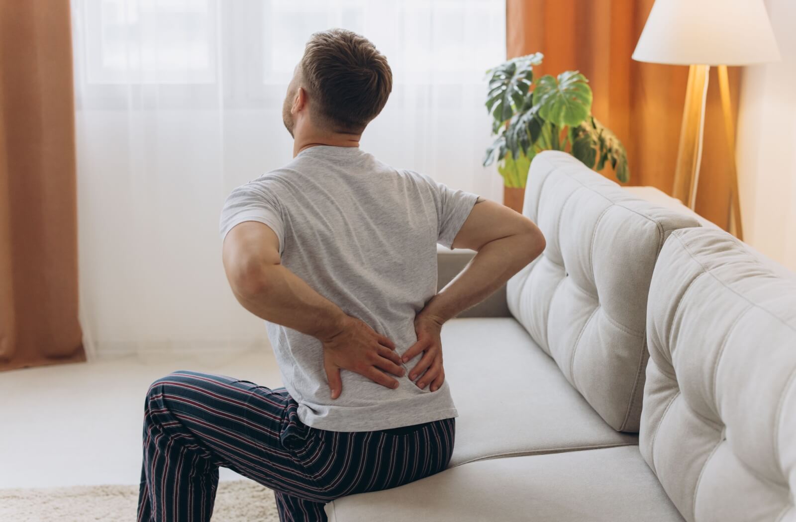 A person sitting on a couch holding their lower back due to pain from sciatica.